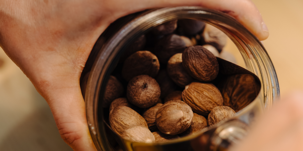 1 ► Place des Epices Close-up of hands tilting a glass jar and pouring almonds into a container.