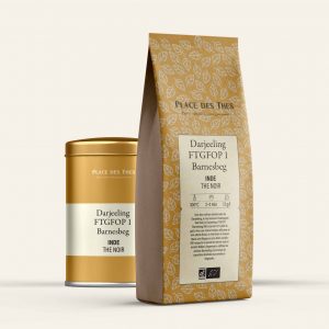 Gold tin and leaf-patterned paper bag for Darjeeling tea, with FTGFOP1 Barnesbeg labeling visible on the front container and bag.